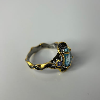 Gold and silver ring with blue gemstone on a gray background