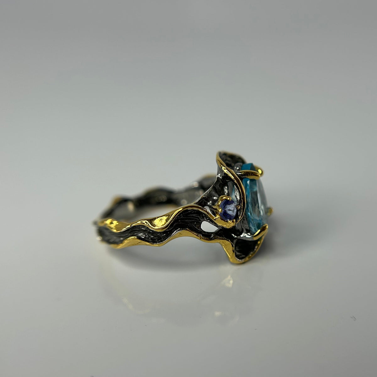 Gold and silver ring with a blue gemstone on a gray background