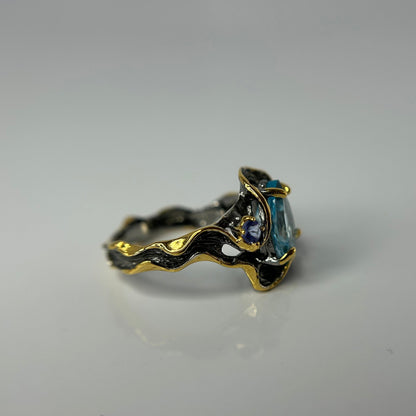 Gold and silver ring with a blue gemstone on a gray background