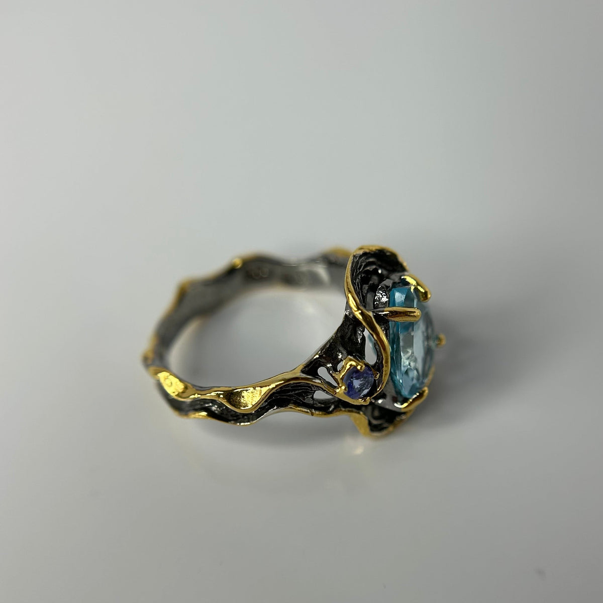 Gold and silver ring with a blue topaz gemstone on a gray background