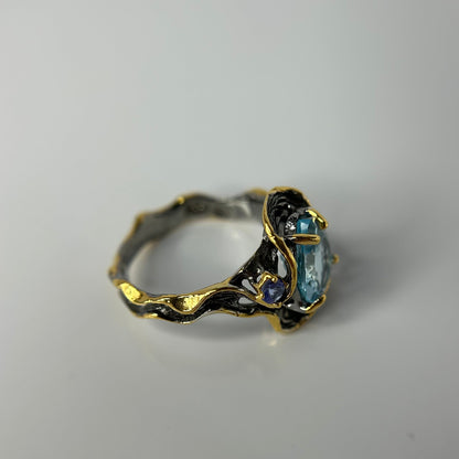 Gold and silver ring with a blue topaz gemstone on a gray background