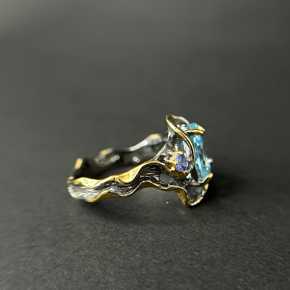 Gold and silver ring with gemstones on a dark gray background