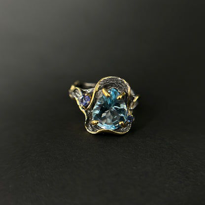 Gold and silver ring with a blue topaz gemstone on a black background
