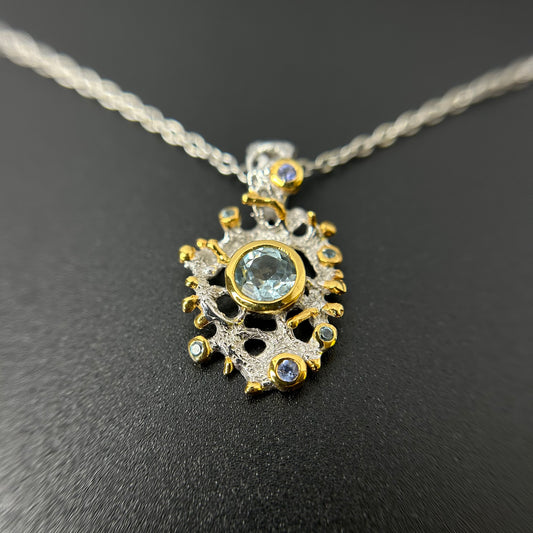 Gold and silver pendant with Topaz gemstones on a chain against a dark background