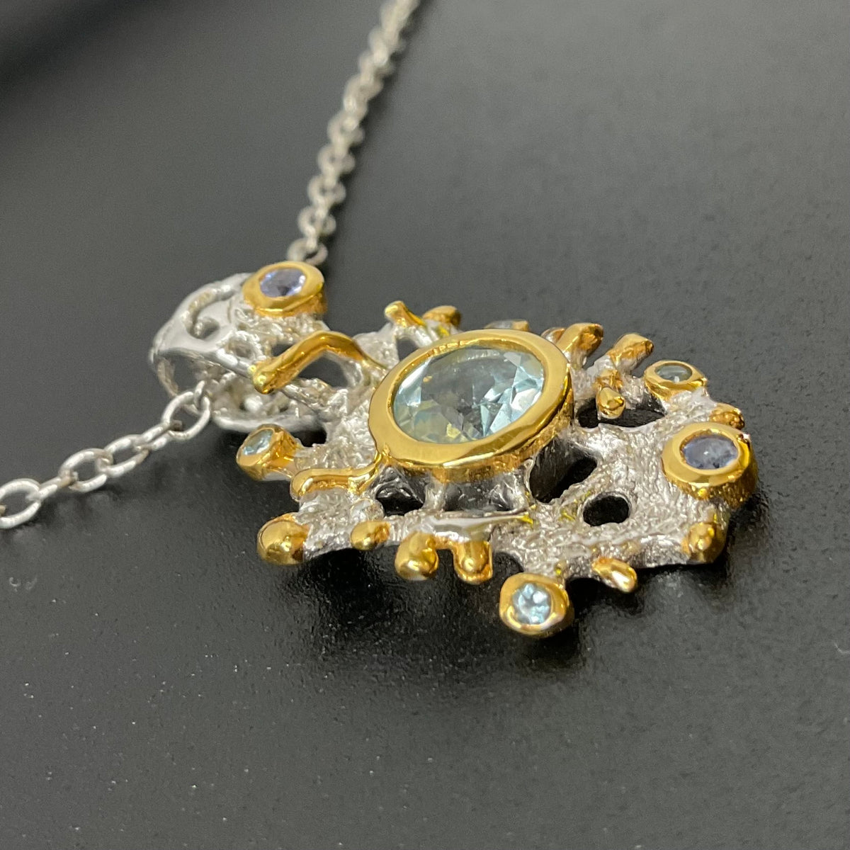 Gold and silver pendant with central Swiss Topaz gemstone on a dark background