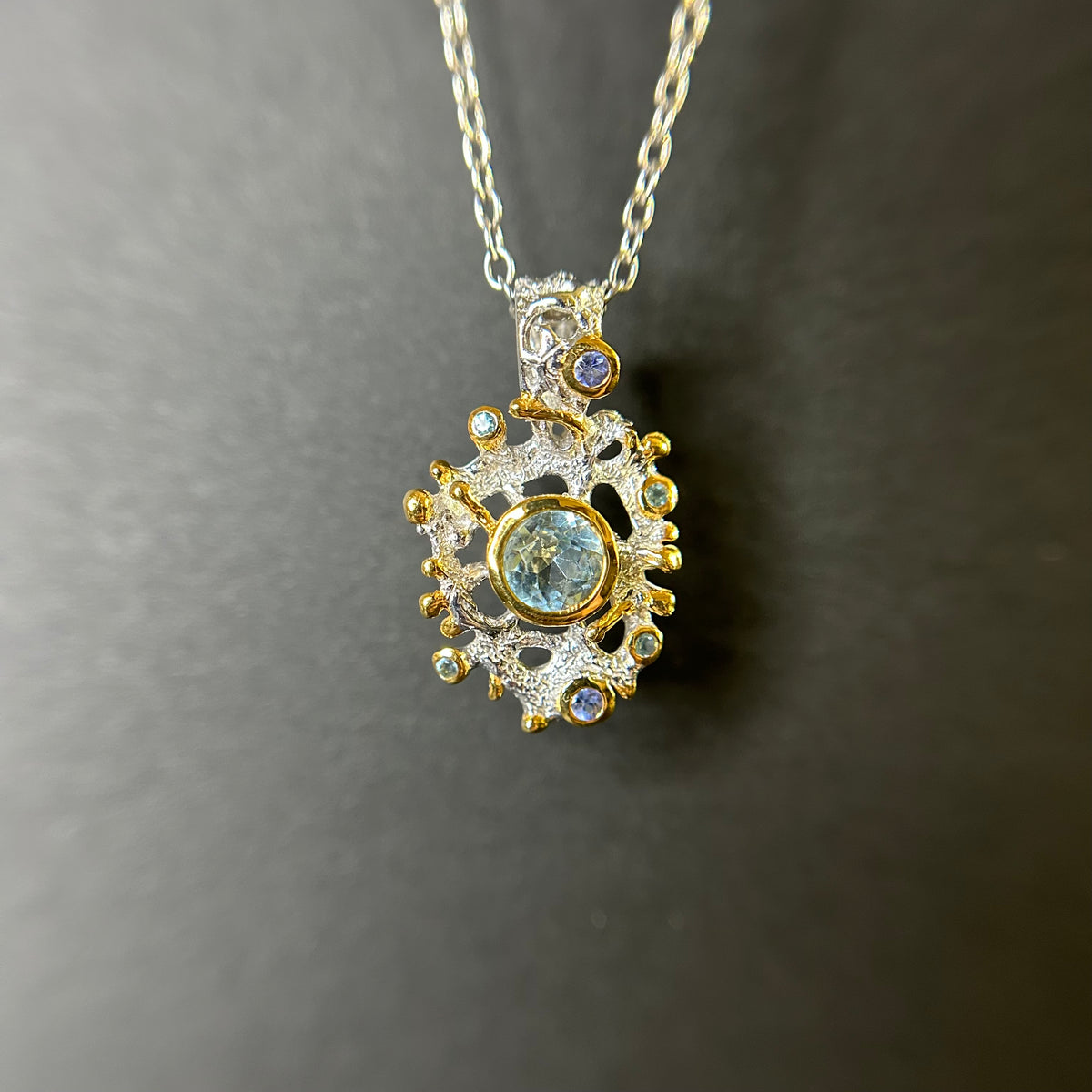 Gold and silver pendant with central Swiss Topaz gemstone on a dark background