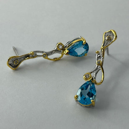 Pair of gold and silver earrings with blue topaz gemstones on a light gray background