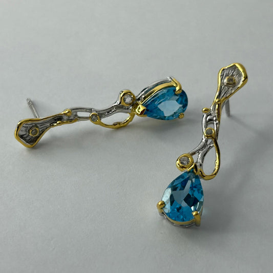 Pair of gold and silver earrings with blue topaz gemstones on a light gray background