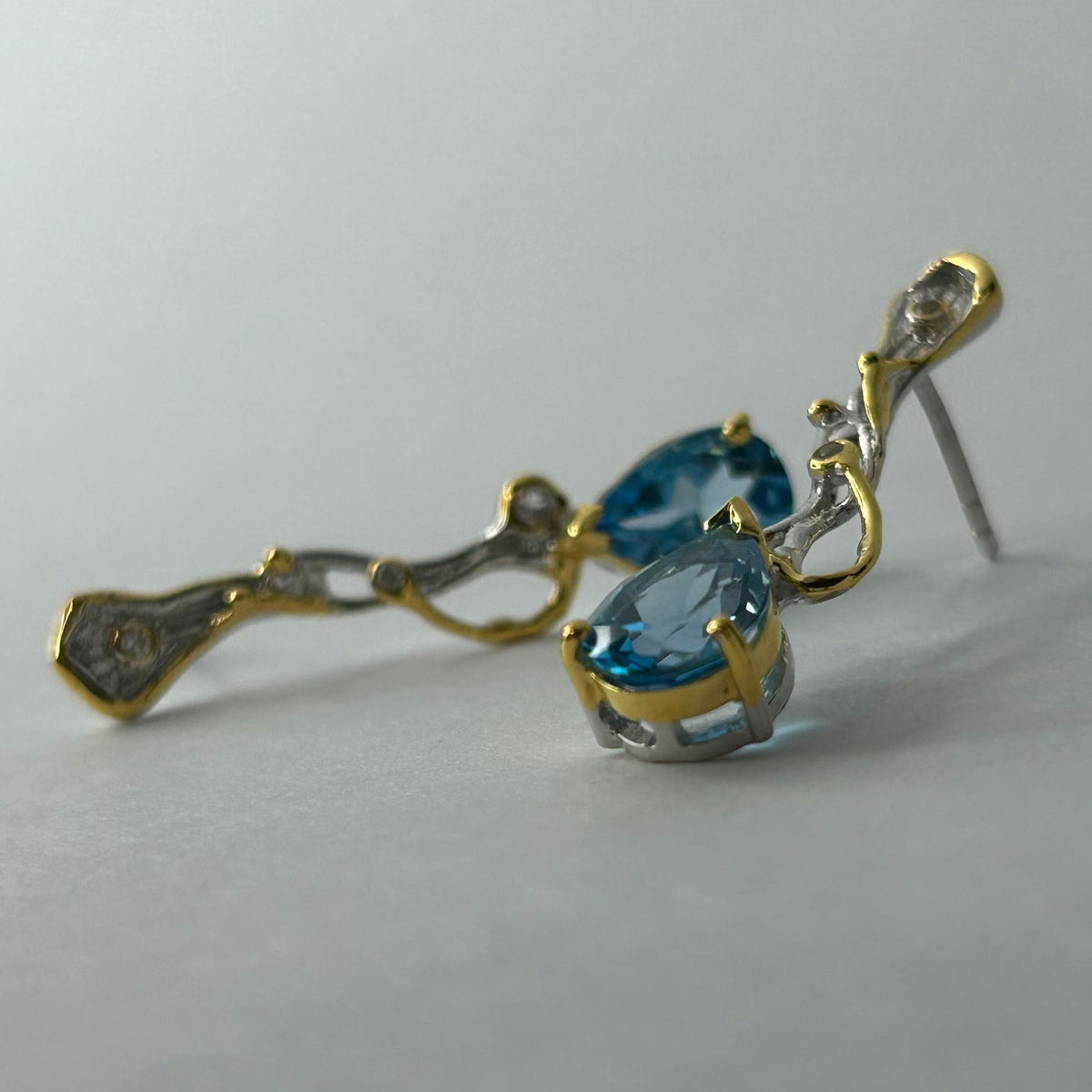 Gold and silver earrings with blue topaz gemstones on a light gray background