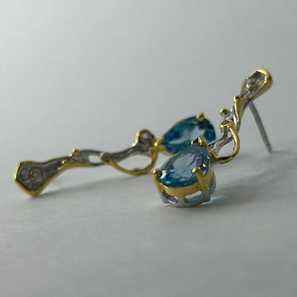 Gold and silver earrings with blue topaz gemstones on a light gray background