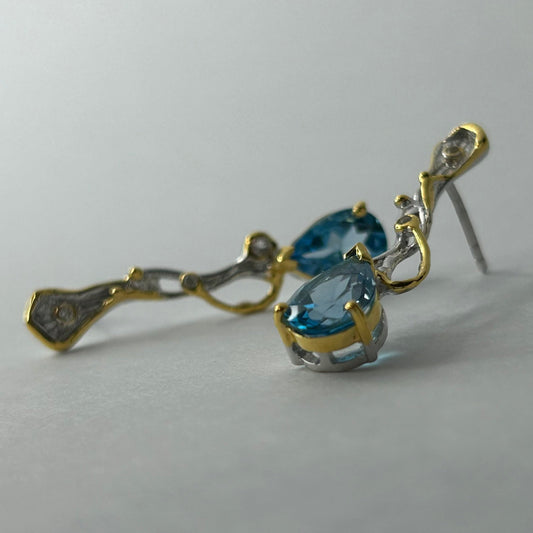 Gold and silver earrings with blue topaz gemstones on a light gray background