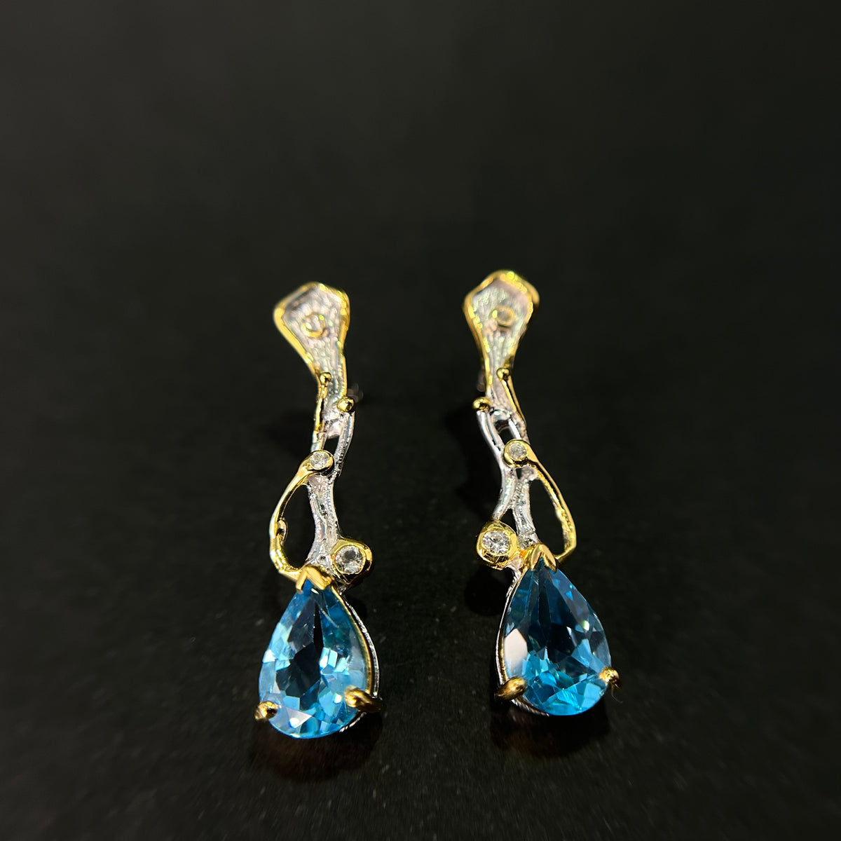 Pair of gold and silver earrings with blue topaz gemstones on a black background