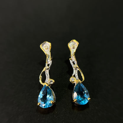 Pair of gold and silver earrings with blue topaz gemstones on a black background
