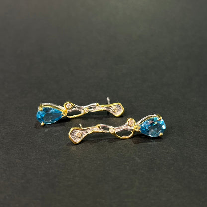 Pair of gold and silver earrings with blue topaz gemstones on a black background