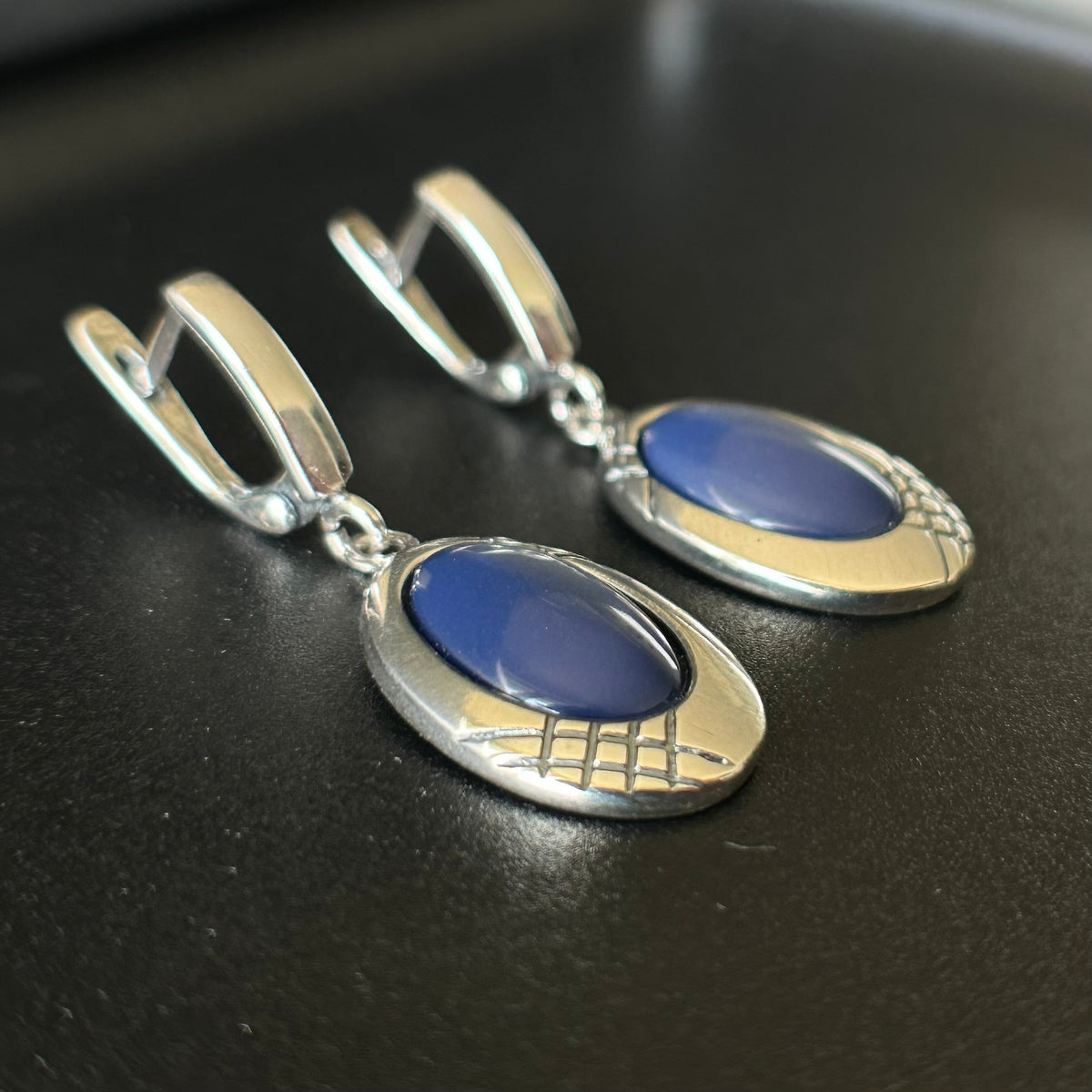 Pair of silver earrings with blue stones on a dark surface