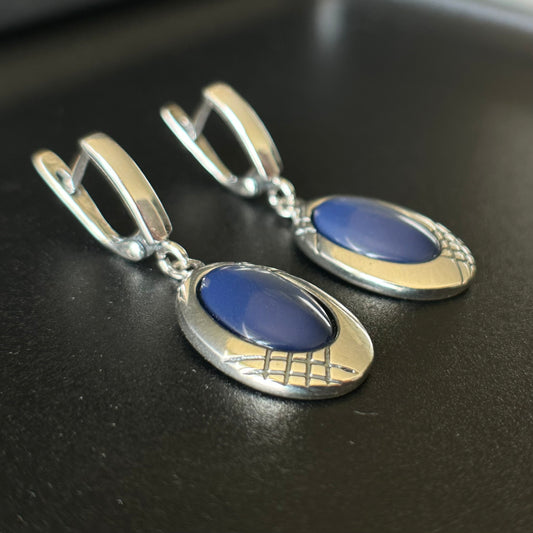 Pair of silver earrings with blue stones on a dark surface