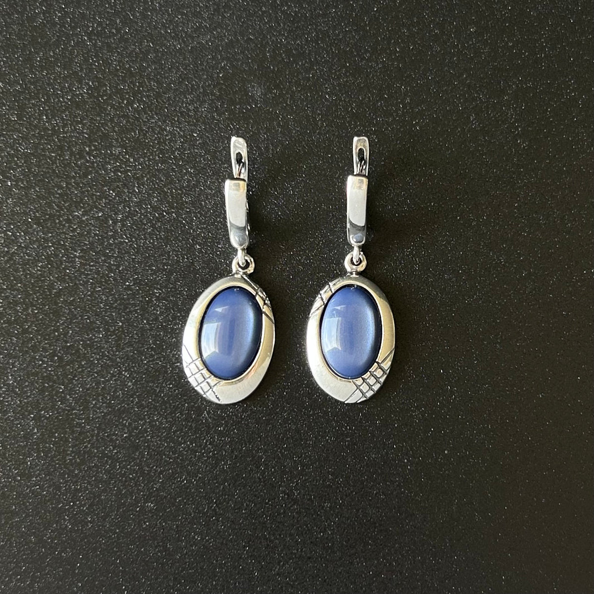 Pair of silver earrings with blue stones on a black background
