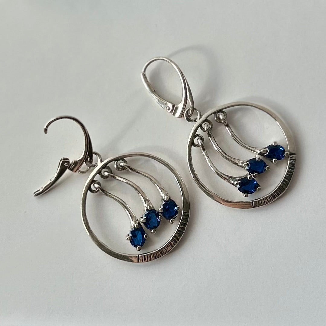 Pair of silver earrings with blue stones on a white background