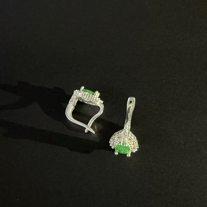 A pair of silver earrings with oval green gemstones surrounded by clear crystals, displayed on a dark reflective surface.