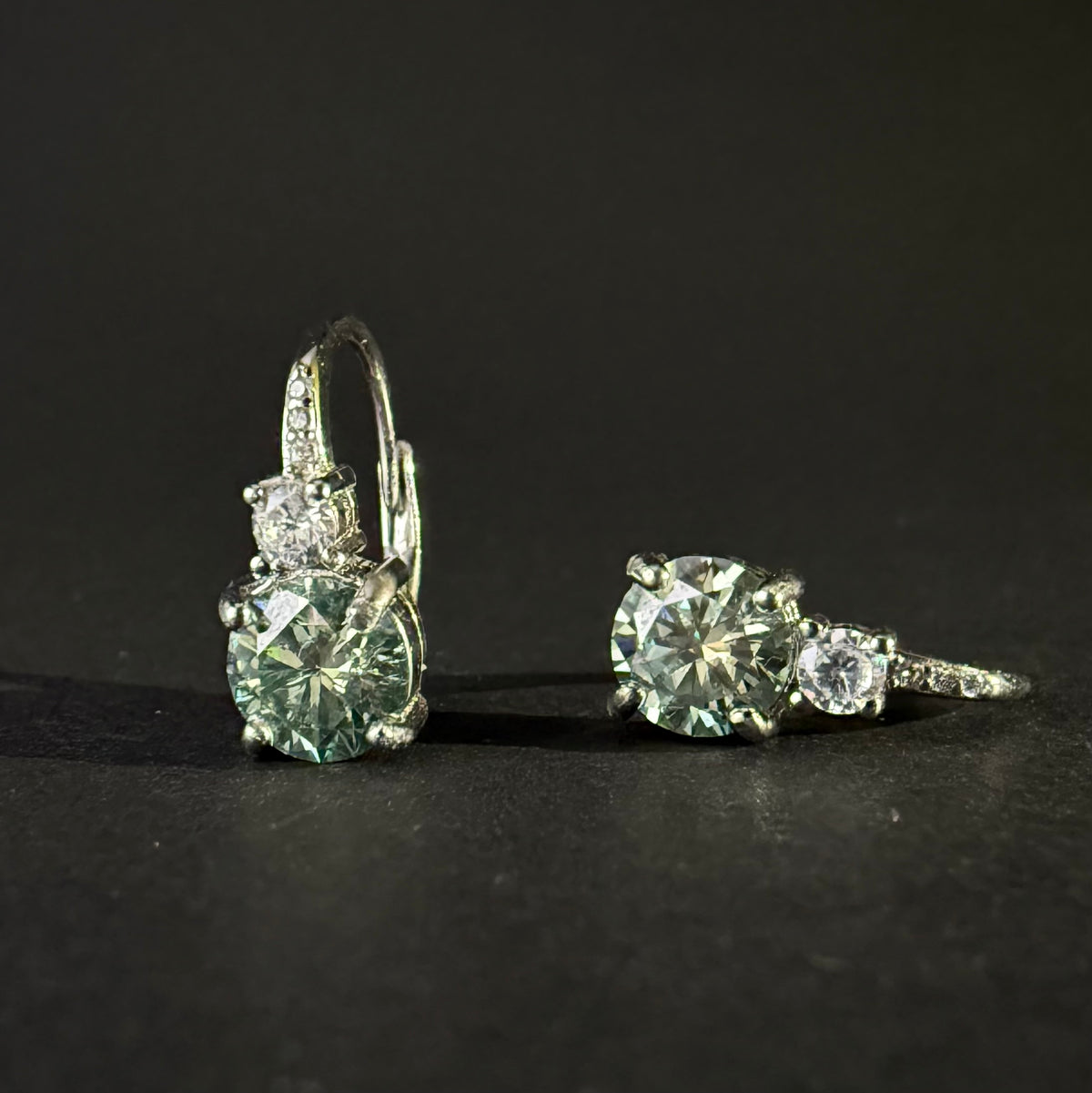 A pair of silver leverback earrings with large round-cut light blue-green moissanite and smaller clear stones.