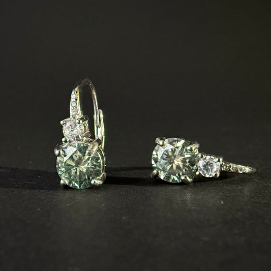 A pair of silver leverback earrings with large round-cut light blue-green moissanite and smaller clear stones.