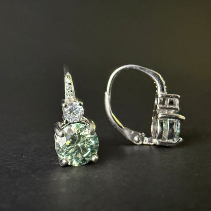A pair of silver leverback earrings with large round-cut light blue-green moissanite and smaller clear stones.