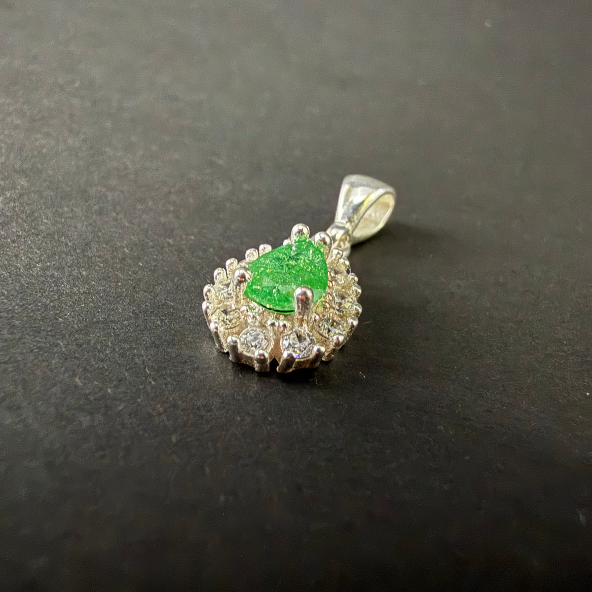 A silver pendant featuring a central green teardrop-shaped gemstone surrounded by a halo of small clear stones