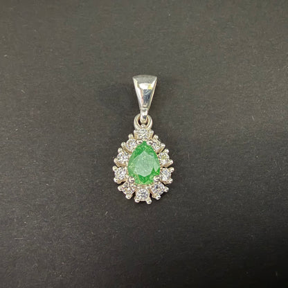 A silver pendant featuring a central green teardrop-shaped gemstone surrounded by a halo of small clear stones