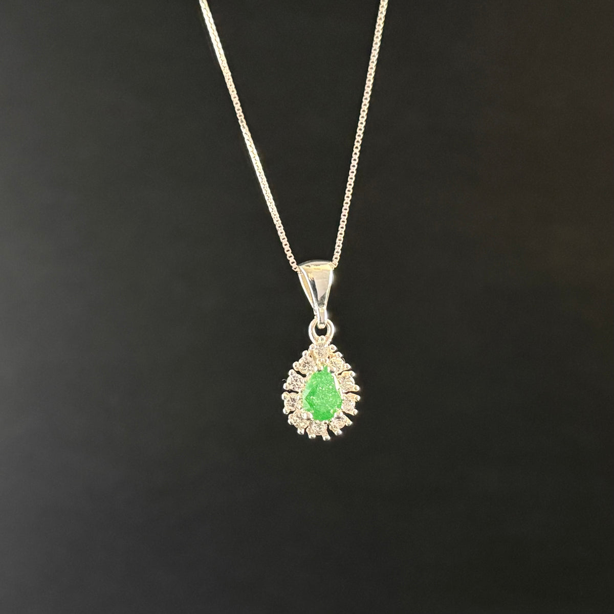 A silver pendant necklace featuring a central green teardrop-shaped gemstone surrounded by a halo of small clear stones