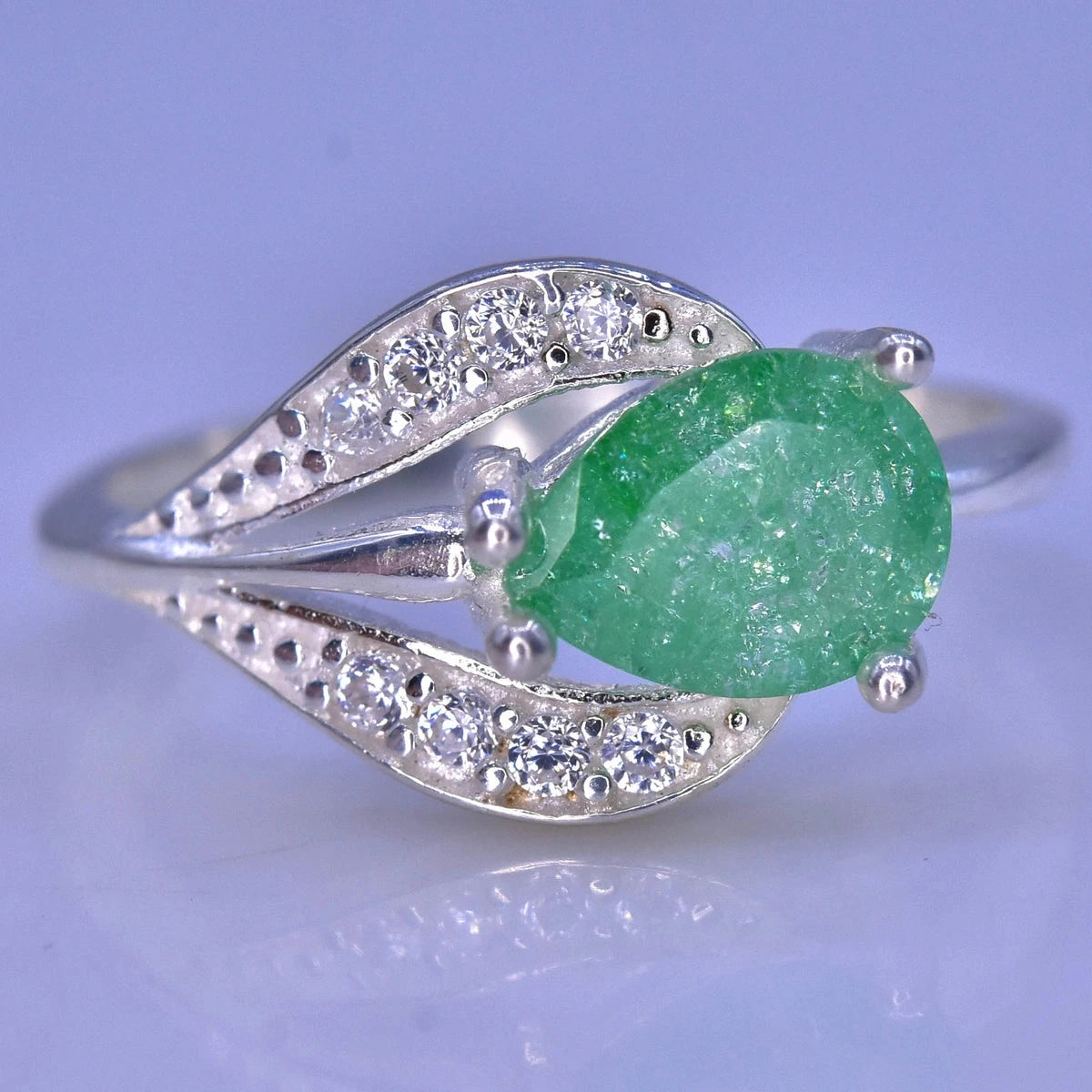 A silver ring featuring a large, faceted green gemstone in an oval shape, surrounded by small clear stones set in a leaf-like design