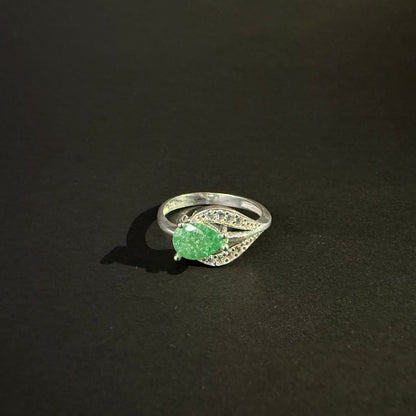 A silver ring featuring a large, faceted green gemstone in an oval shape, surrounded by small clear stones set in a leaf-like design